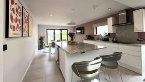 A modern kitchen with a central island, white cabinetry, and a large window providing natural light. - Luxury Family Home in Central Windsor with Large Garden, Games Room & Parking (Windsor)