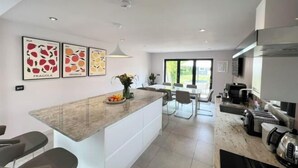 A modern kitchen with a central island, white cabinetry, and a dining area with a large window. - Luxury Family Home in Central Windsor with Large Garden, Games Room & Parking (Windsor)