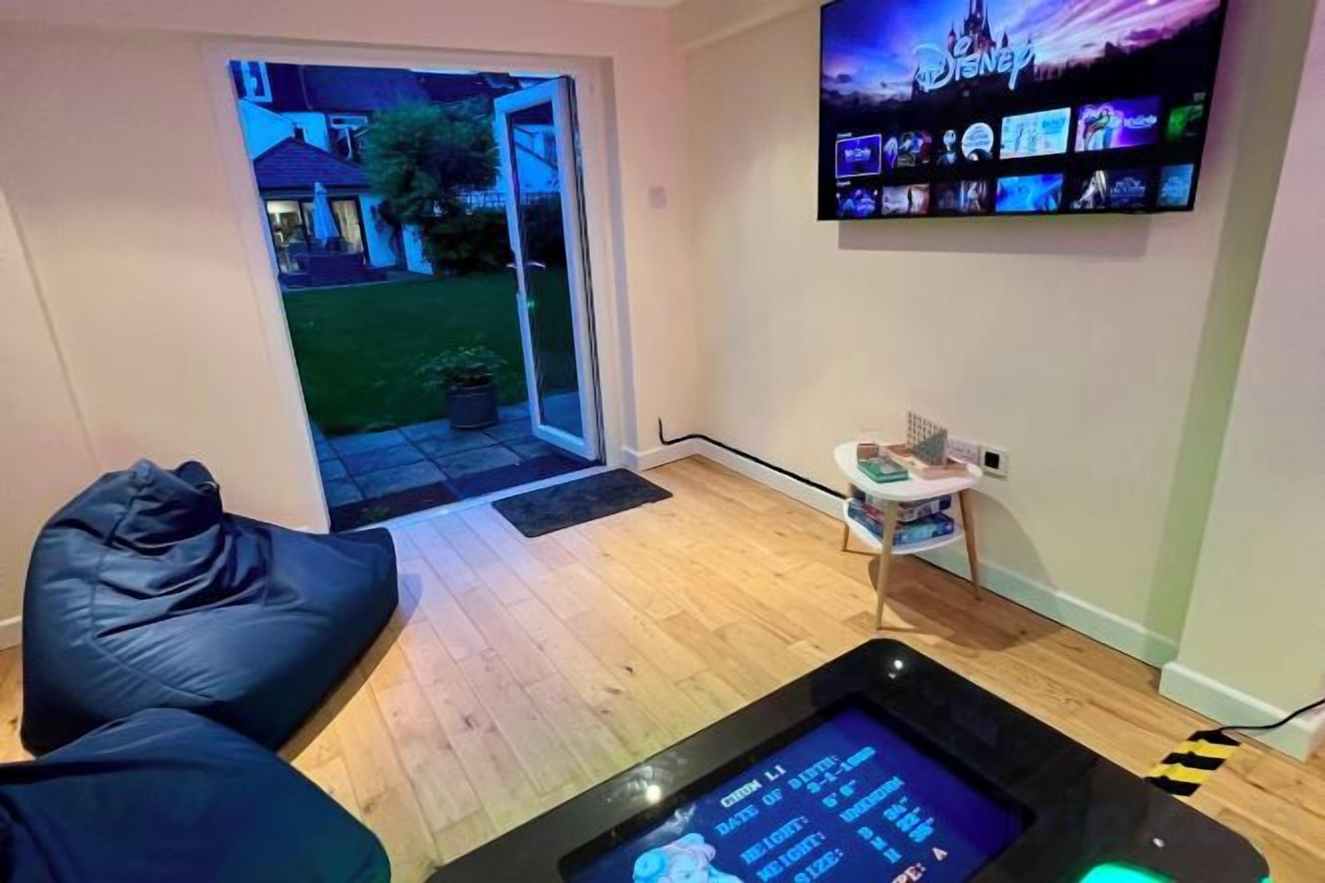 Una habitación con una gran televisión de pantalla plana montada en la pared, un sillón informal, una mesita con una planta y un ventanal corredero que da a un espacio exterior.