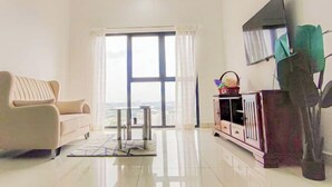 Een moderne woonkamer met een bank, een televisie aan de muur en uitzicht door grote ramen.