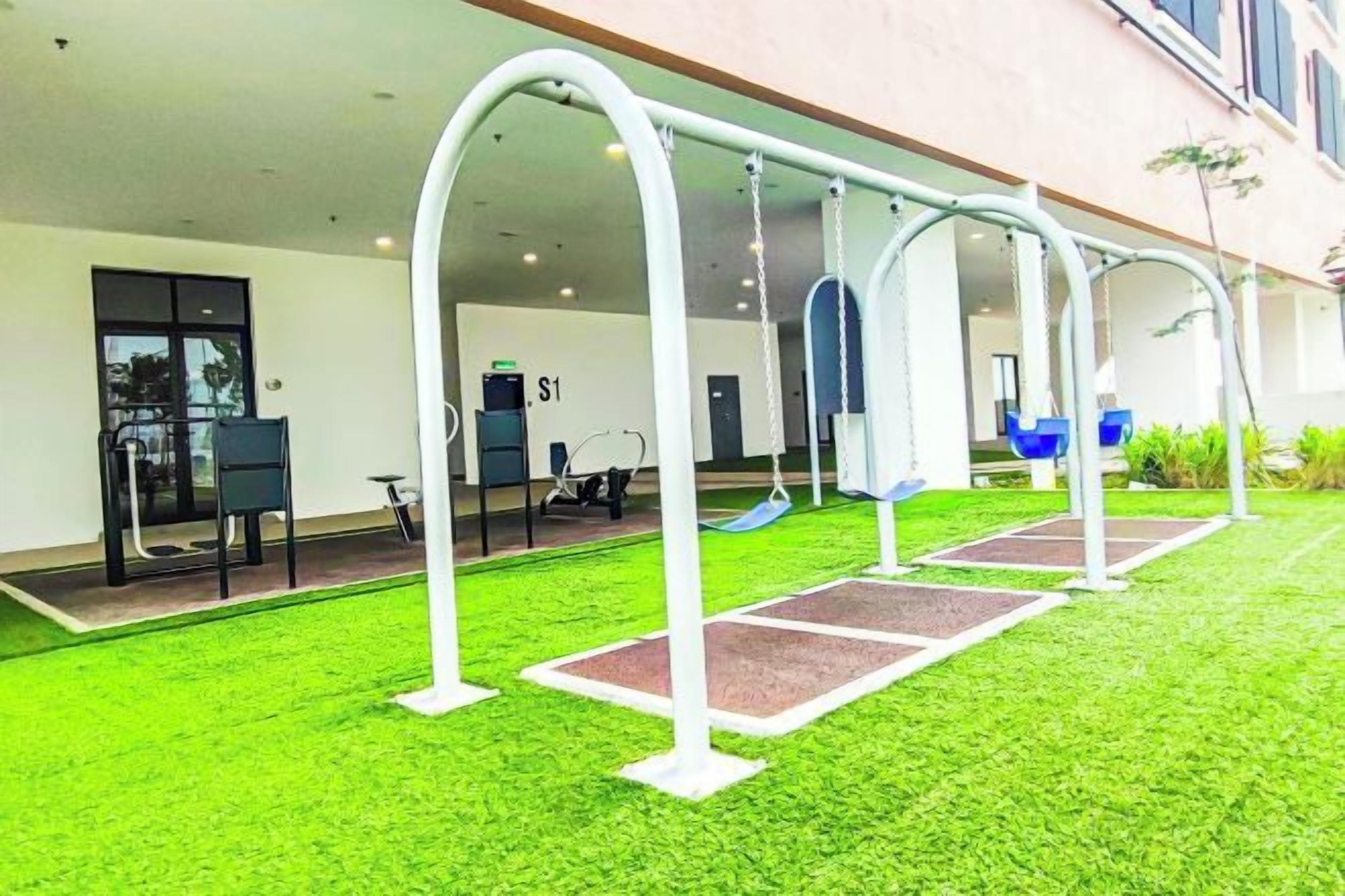 An outdoor area with swings and a slide, a covered seating area, and a building entrance.