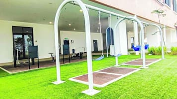 An outdoor area with swings and a slide, a covered seating area, and a building entrance.