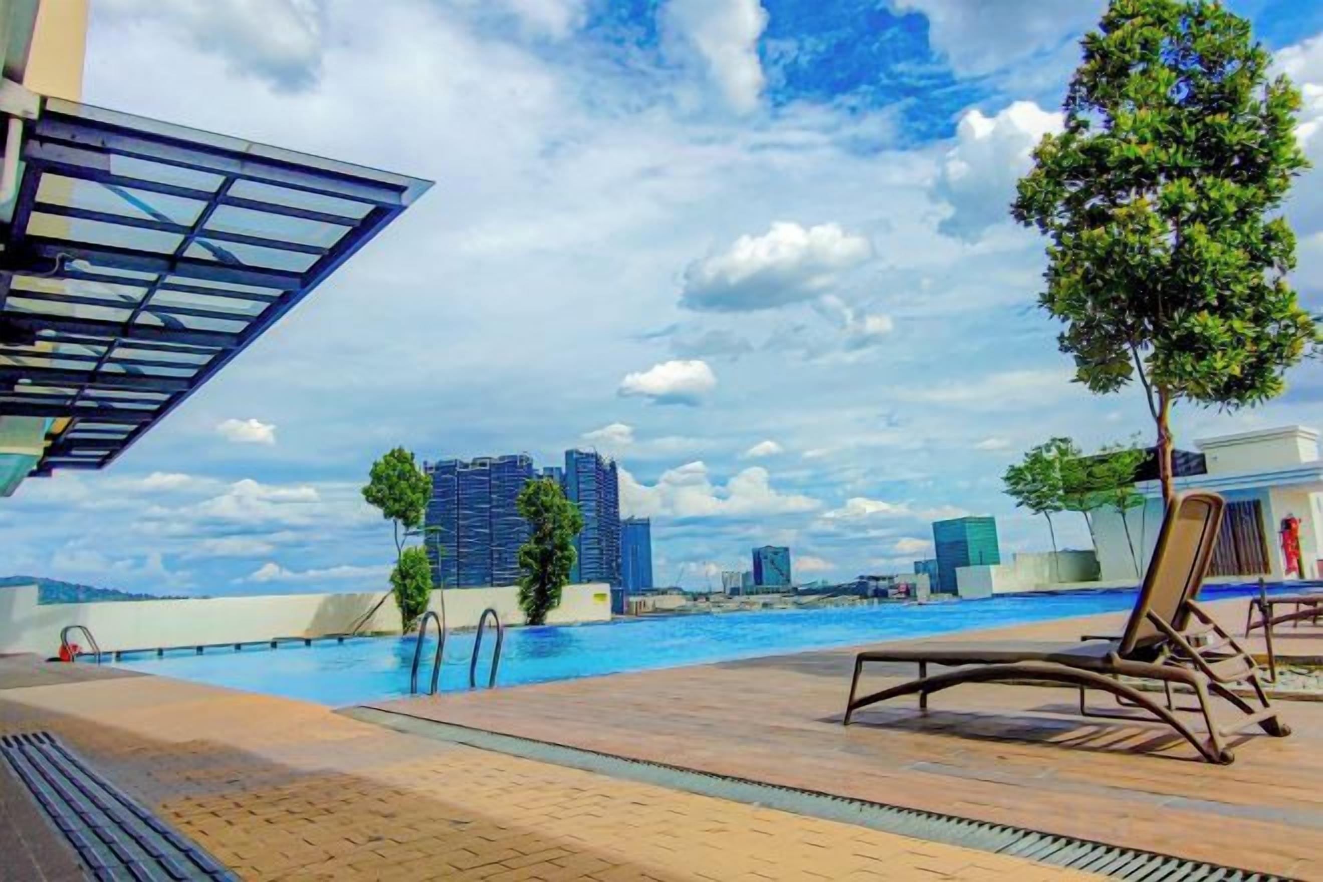 A poolside area with lounge chairs, a tree, and a view of a cityscape with buildings in the background.