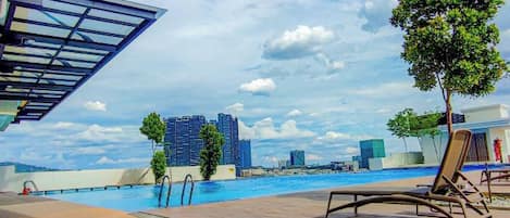 A poolside area with lounge chairs, a tree, and a view of a cityscape with buildings in the background.