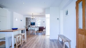 Une cuisine spacieuse avec un plancher en bois, un coin repas avec une table et des chaises, et un banc près de la porte.