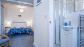 Une chambre à coucher comprenant un lit, une table de chevet, une lampe, ainsi qu’une salle de bain avec un lavabo et une douche.
