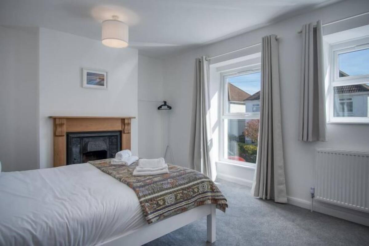 Un dormitorio con cama, chimenea, ventana con cortinas y vista al exterior.