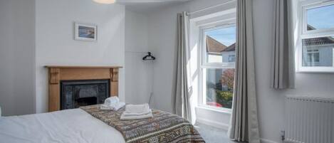 A bedroom with a bed, a fireplace, a window with curtains, and a view of the outside.