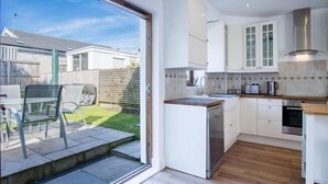 Une cuisine moderne avec des armoires blanches, un four encastré et une grande fenêtre donnant sur un jardin.