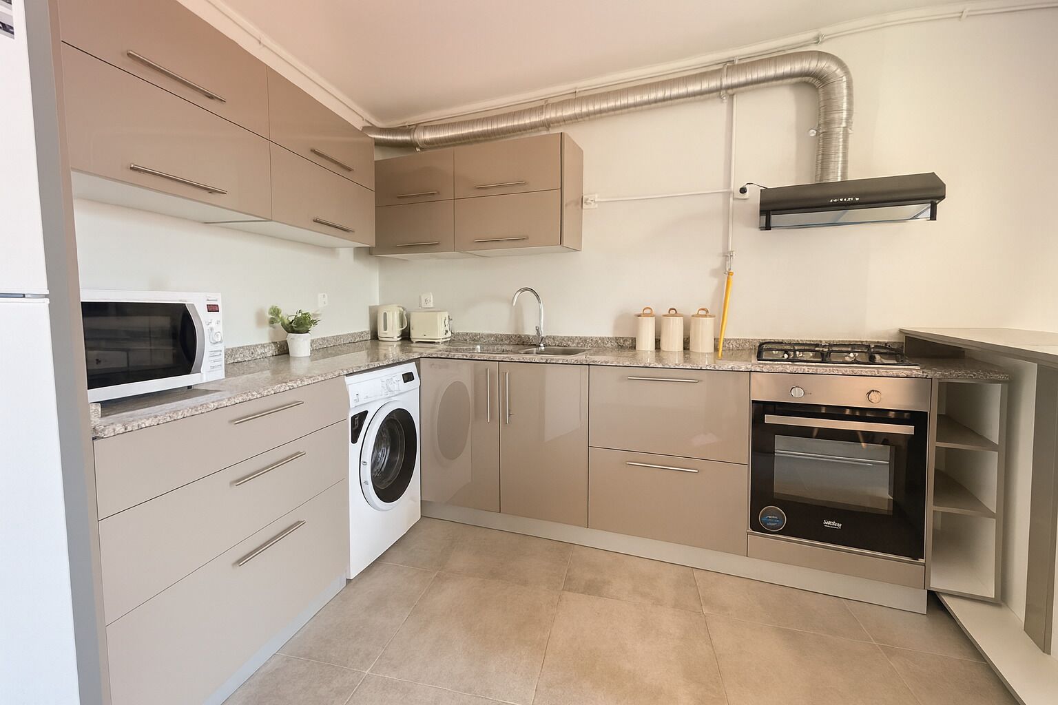 A compact kitchen with a washing machine, microwave, oven, and a built-in stove.
