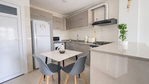 A modern kitchen with a white refrigerator, microwave, stove, and sink. There is a small dining table with two chairs. - Spacieux Appartement a Dely Brahim (Algiers)