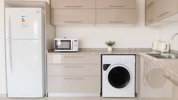 A compact kitchen with a refrigerator, microwave, and washing machine.
