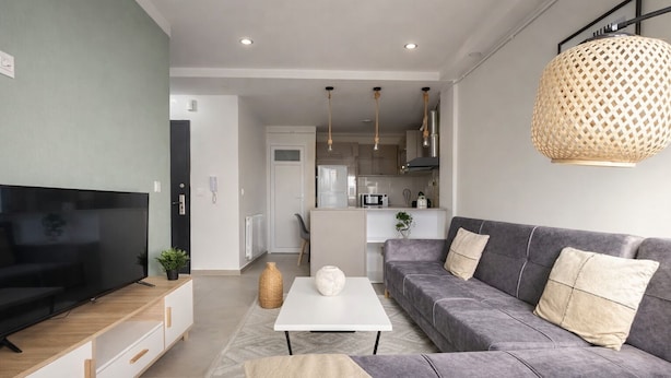A modern living room with a flat-screen TV, grey sofa, white coffee table, and a kitchen in the background. - Spacieux Appartement a Dely Brahim (Algiers)