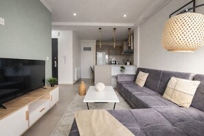 A modern living room with a flat-screen TV, grey sofa, white coffee table, and a kitchen in the background. - Spacieux Appartement a Dely Brahim (Algiers)