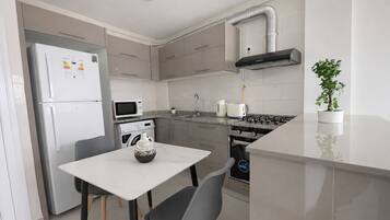 A modern kitchen with a white refrigerator, microwave, oven, and gas stove. There is a small dining table with two chairs.