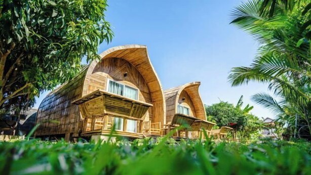 Twee houten boomhuisachtige gebouwen met gebogen daken, omgeven door weelderige begroeiing.