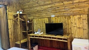 Een kamer met een bamboe wand, een televisie op een houten standaard, een plank met spullen, en een afvalbak.