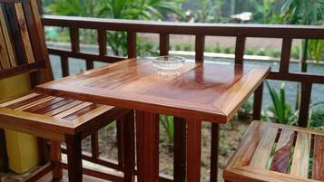 Mesa y sillas de madera en un balcón con vista a follaje y una masa de agua.