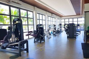 Une salle de sport équipée de divers appareils d’exercice, dotée de grandes fenêtres et d’un plafond haut.