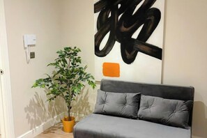 A room with a grey upholstered headboard sofa, a potted plant, and a wall with abstract art. - Beautiful Retreat in the Heart of the City Leeds (Leeds)