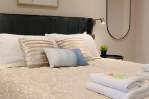 A neatly made bed with a dark headboard, two decorative pillows, and a stack of folded towels. - Beautiful Retreat in the Heart of the City Leeds (Leeds)