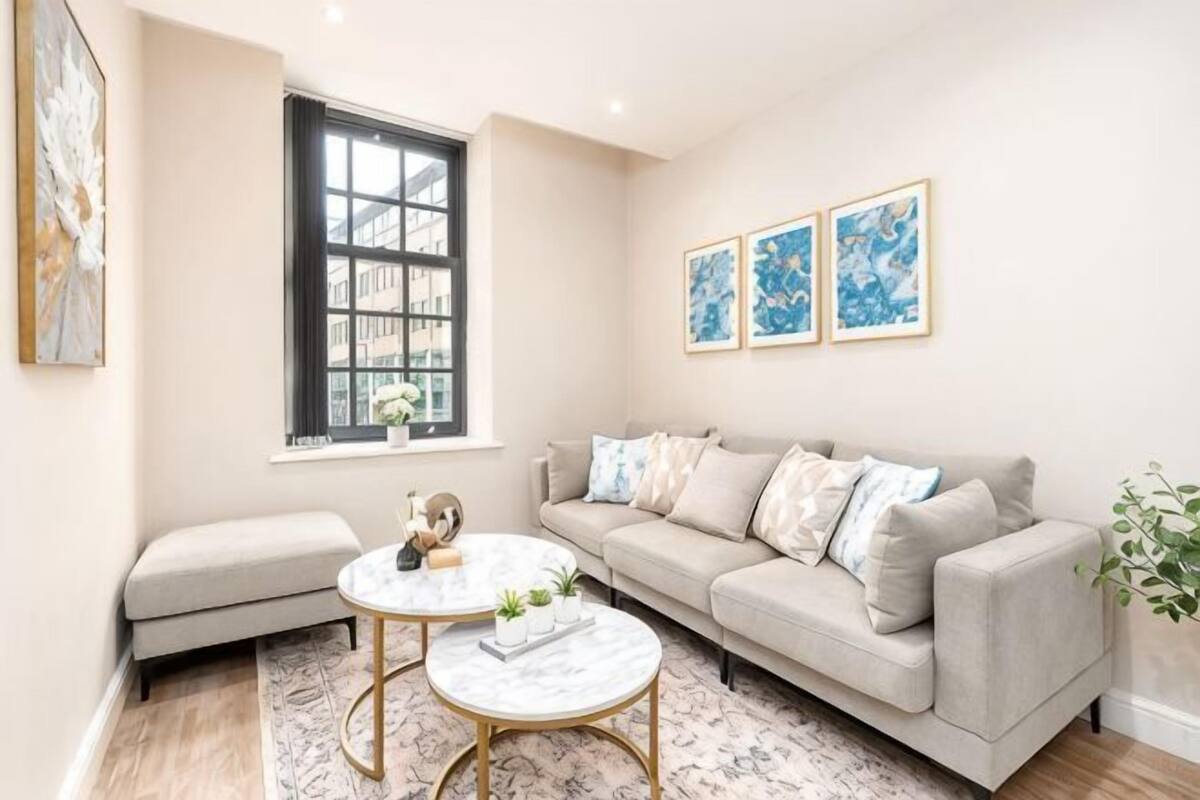 A living room with a sofa, two round tables, a window, and framed artwork on the wall.