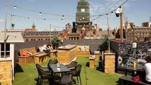A rooftop terrace with wooden furniture, string lights, and a view of the city skyline. - Beautiful Retreat in the Heart of the City Leeds (Leeds)