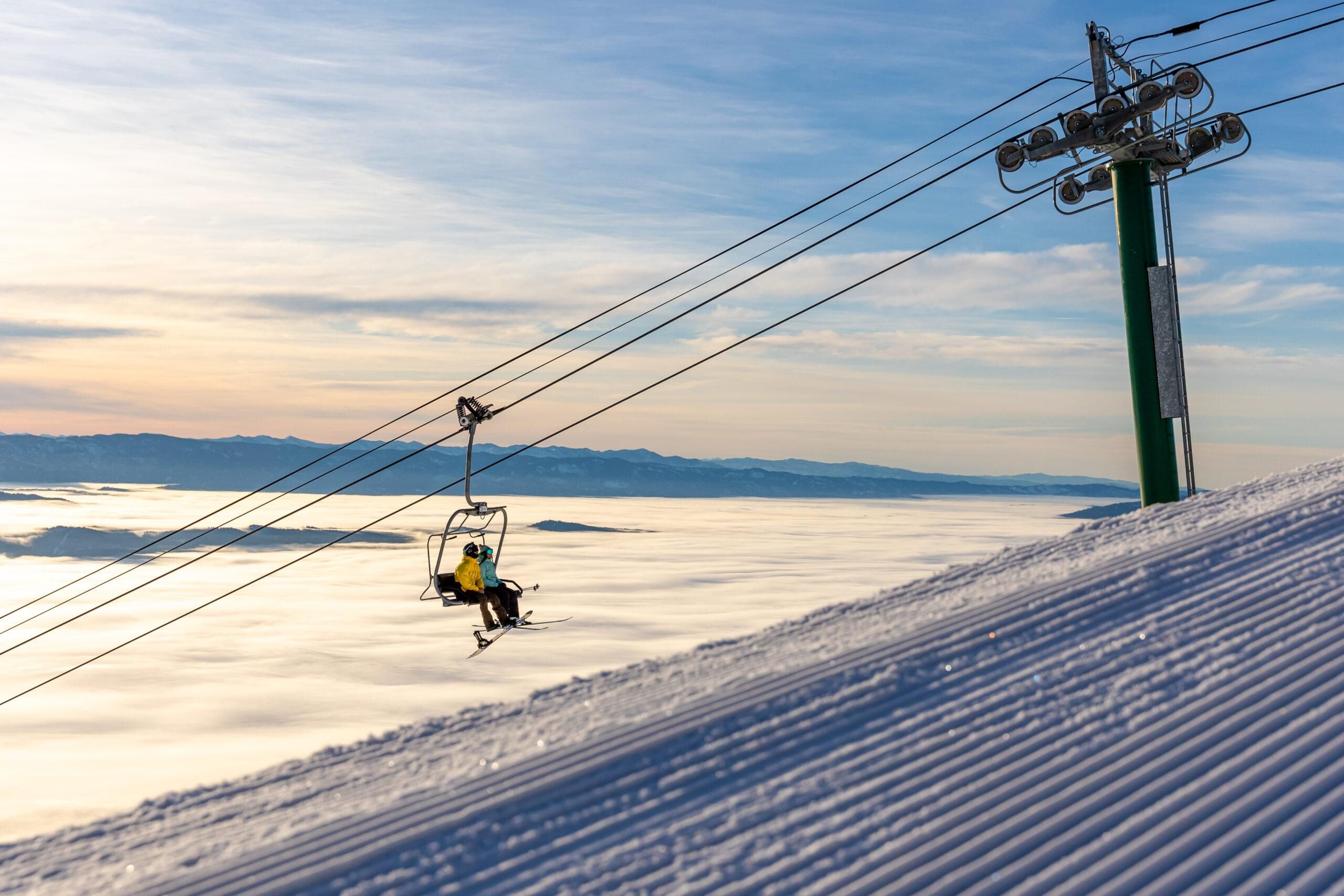 A ski lift with passengers, a snowy mountain slope, and a clear sky.