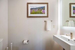 Une salle de bain avec un tableau représentant des fleurs accroché au mur, un porte-serviettes avec une serviette, un porte-rouleau de papier toilette et un lavabo avec un robinet.
