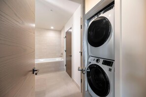 A laundry room with two front-loading washing machines and a bathtub.