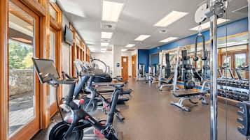 Et fitnesscenter med træningsudstyr, store vinduer og udsigt til det fri.