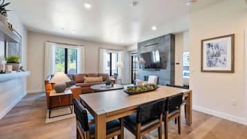 A modern living room with a wooden dining table, leather sofa, and a TV mounted on the wall.