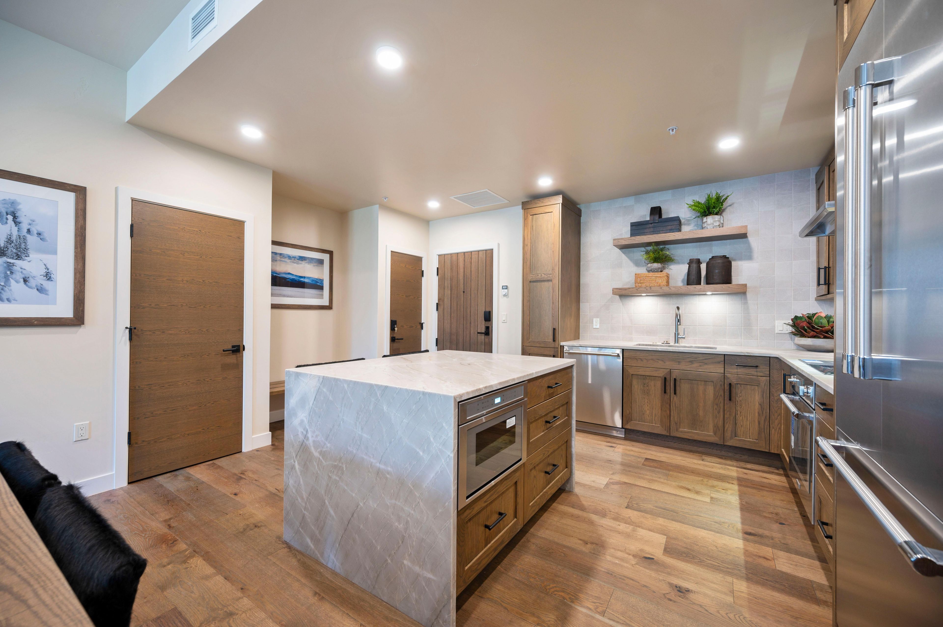A modern kitchen with wooden cabinets, a marble island, stainless steel appliances, and a built-in oven.