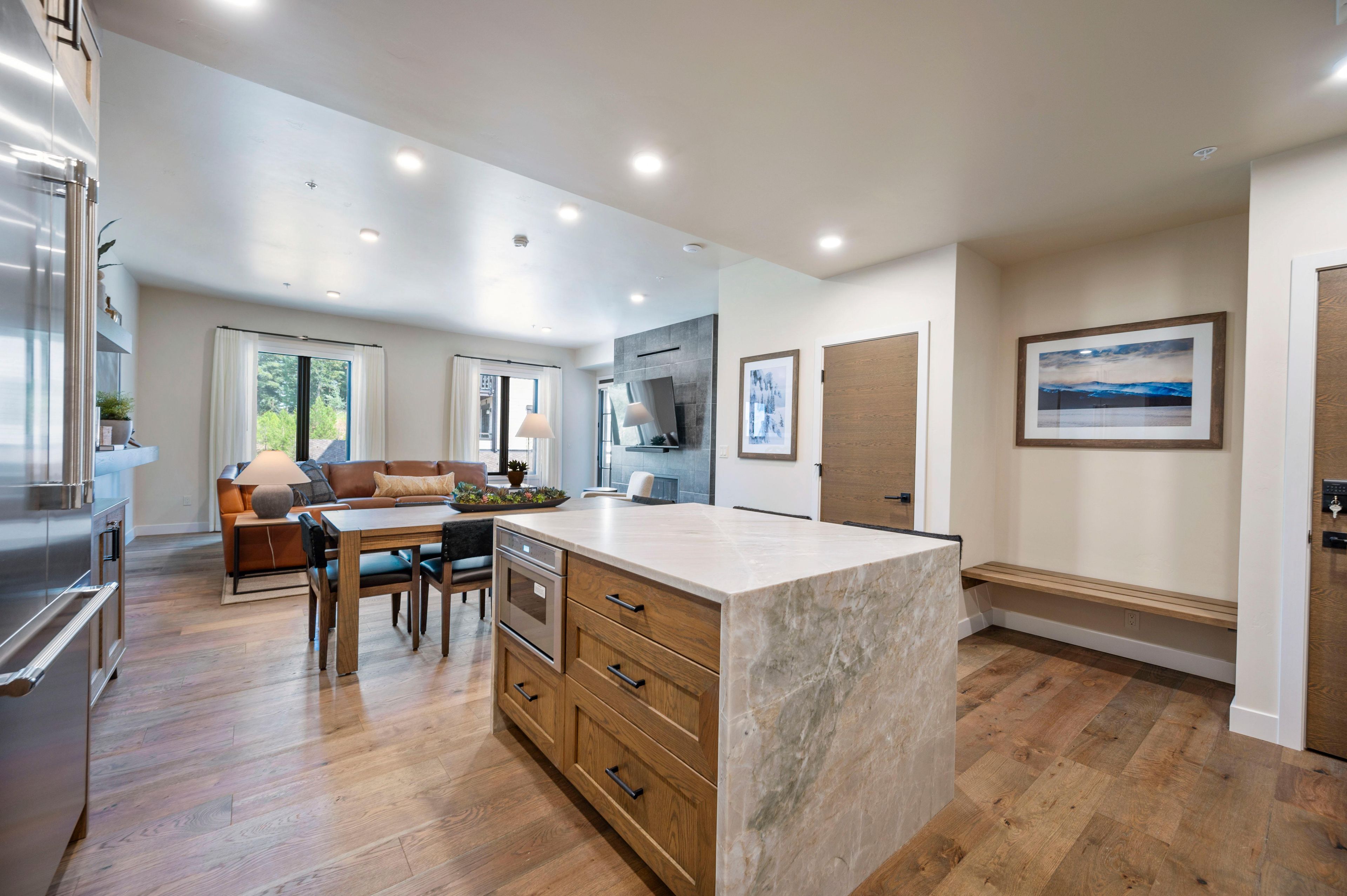 A modern kitchen with wooden cabinets, a marble island, and a dining area with a sofa and table.