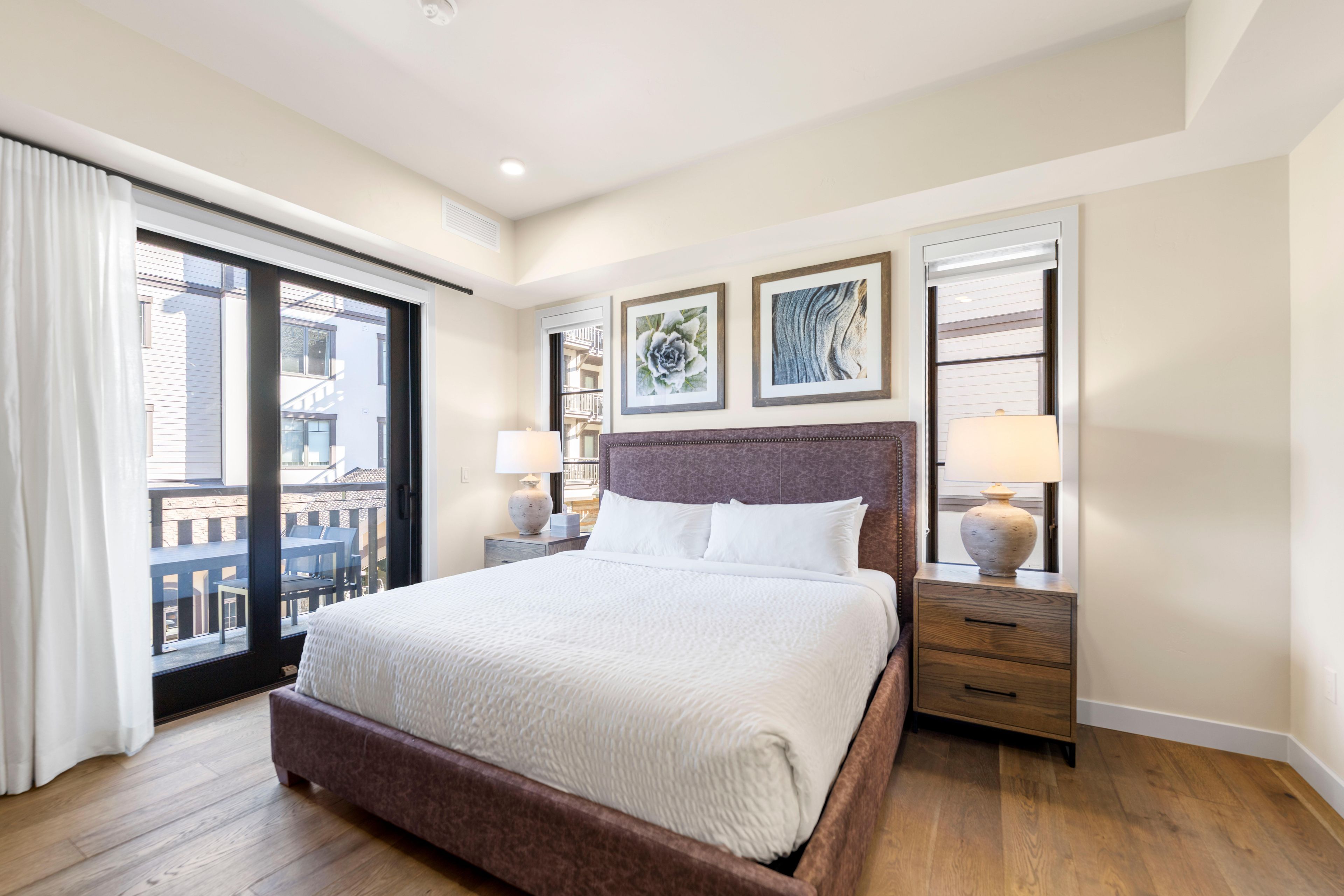 A hotel room with a large bed, a balcony, and two bedside tables with lamps.