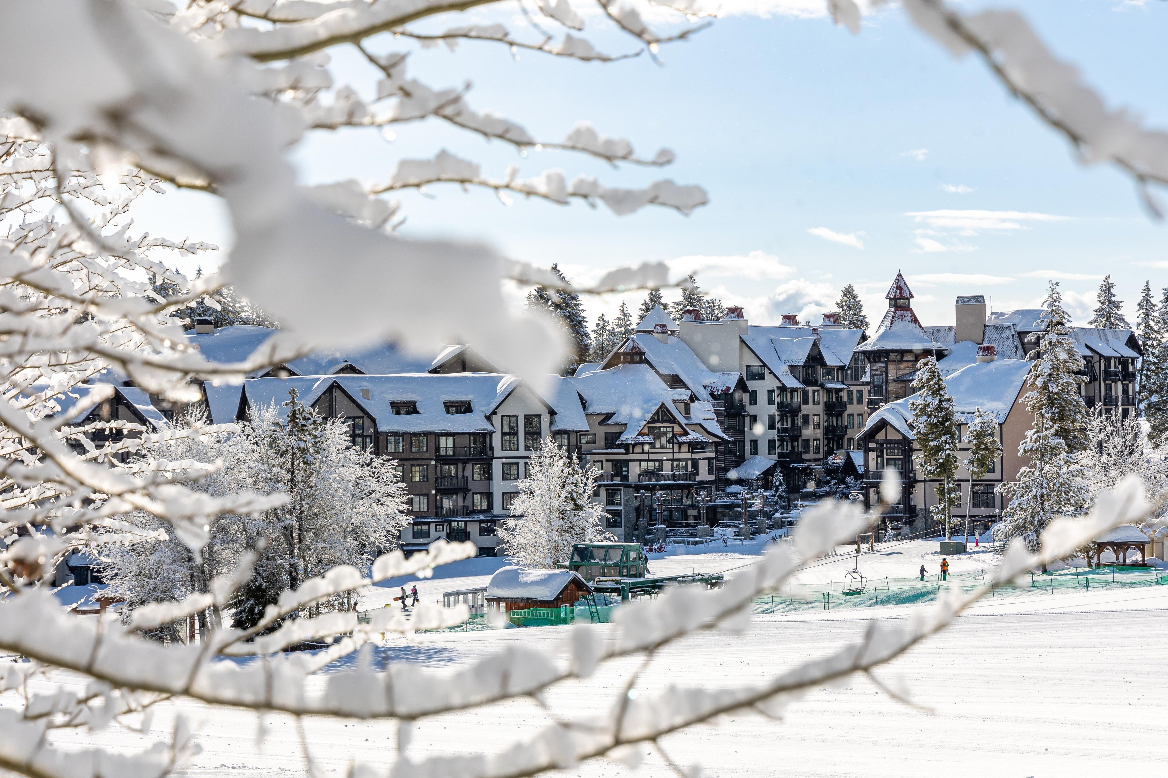 Ein mit Schnee bedeckter Gebäudekomplex mit mehreren Gebäuden, darunter ein großes Hotel mit mehreren Stockwerken und ein kleineres Gebäude mit einem grünen Dach.