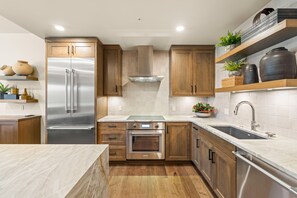 Cozinha moderna com armários de madeira, eletrodomésticos de aço inoxidável e bancada de mármore.