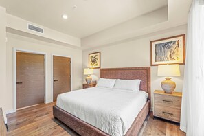 Ein Hotelzimmer mit einem großen Bett, zwei Nachttischen mit Lampen, einer Kopfteil und zwei Türen.