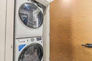 Een gestapelde wasmachine en droger met een bedieningspaneel en een houten deur.