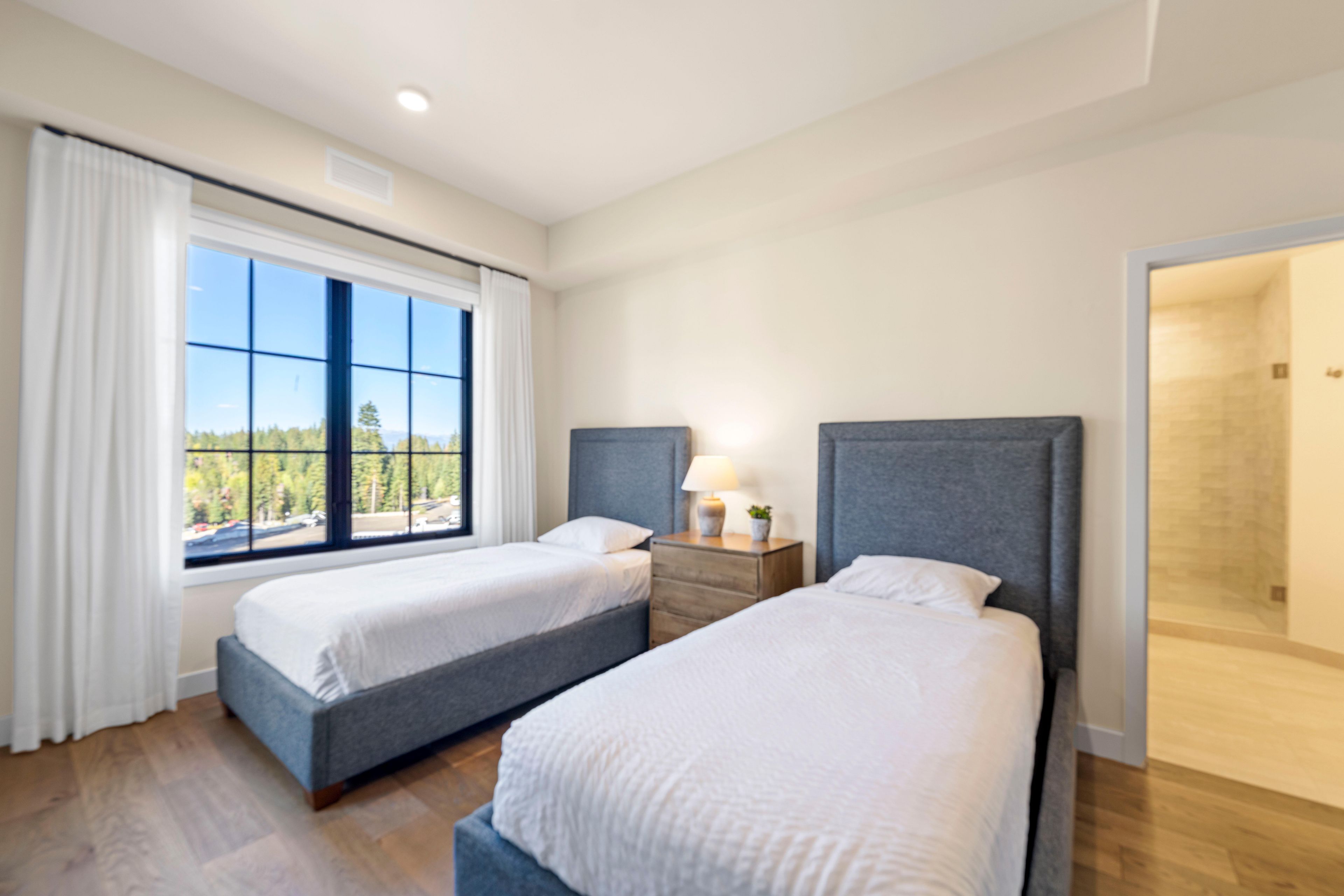 Une chambre d’hôtel avec deux lits, une fenêtre donnant sur un beau paysage, une table de chevet avec une lampe et une porte menant à la salle de bain.