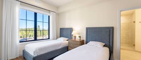 Habitación de hotel con dos camas, una ventana con vistas, una mesita de noche con lámpara y una puerta que da a un baño.