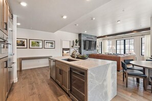 Una cocina moderna con una isla de mármol, armarios de madera y una zona de comedor con mesa y sillas.