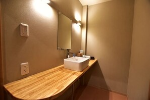 Baño con tocador de madera, lavamanos blanco, espejo y lámpara.