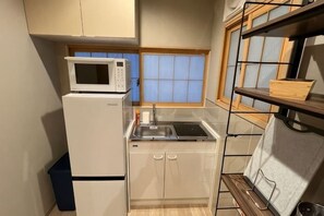 Una cocina compacta con microondas, refrigerador, lavamanos y ventana de madera.