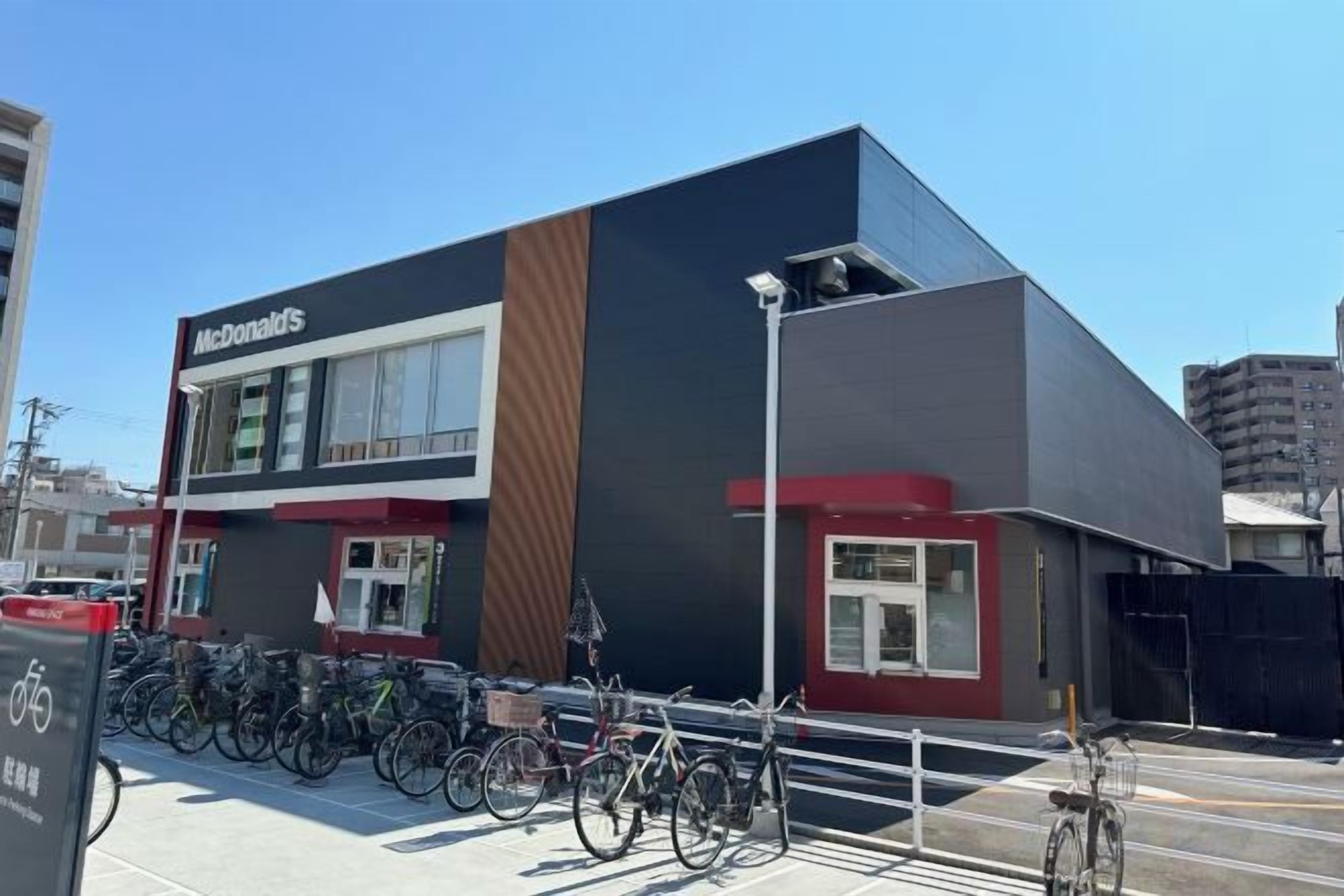 A McDonald's restaurant with a modern design, featuring a prominent logo, a bike parking area, and a clear sky.