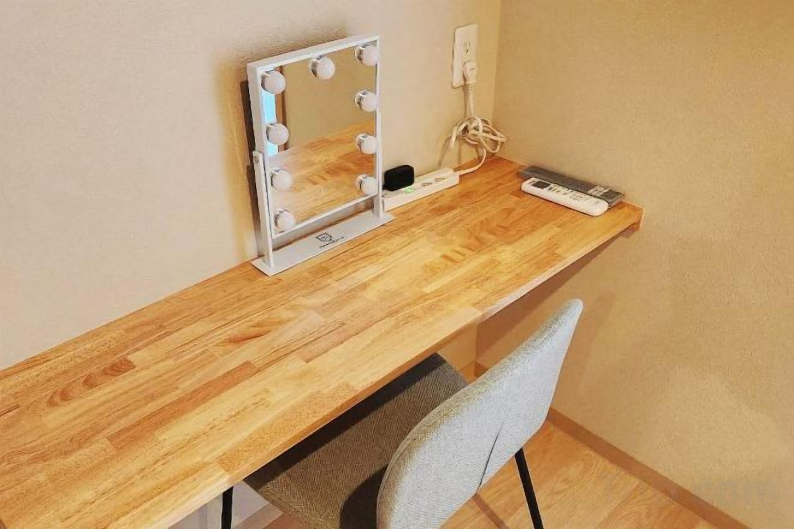 A wooden desk with a mirror and lights, a chair, and a power outlet.