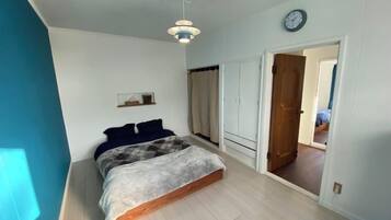 A bedroom with a bed, a bedside table, a wardrobe, and a door leading to another room.