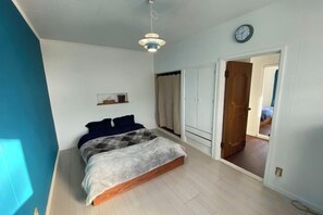 A bedroom with a bed, a bedside table, a wardrobe, and a door leading to another room. - Poroto Base (Shiraoi)