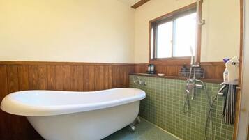 A bathroom with a freestanding bathtub, a window, and a tiled wall.