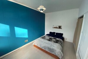 Un dormitorio con una cama, un tabique azul, una lámpara en el techo y un estante con objetos.